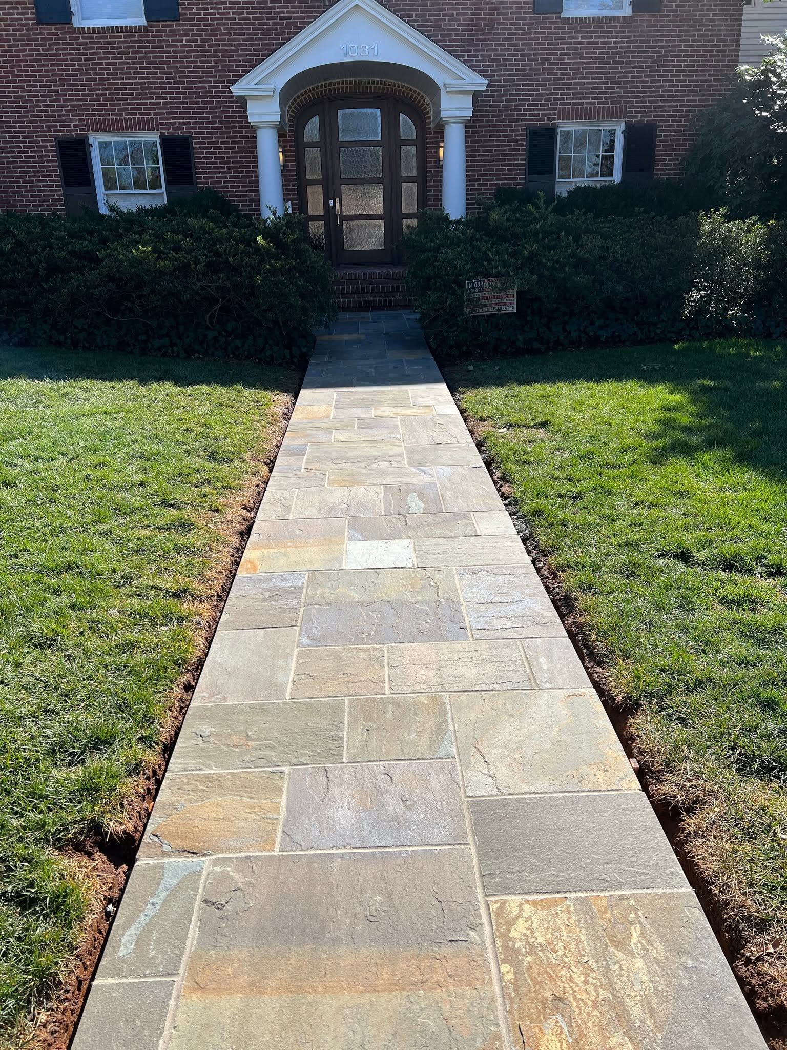 Stone walkway leading to a brick house with a dark front door and white trim, bordered by green lawn.