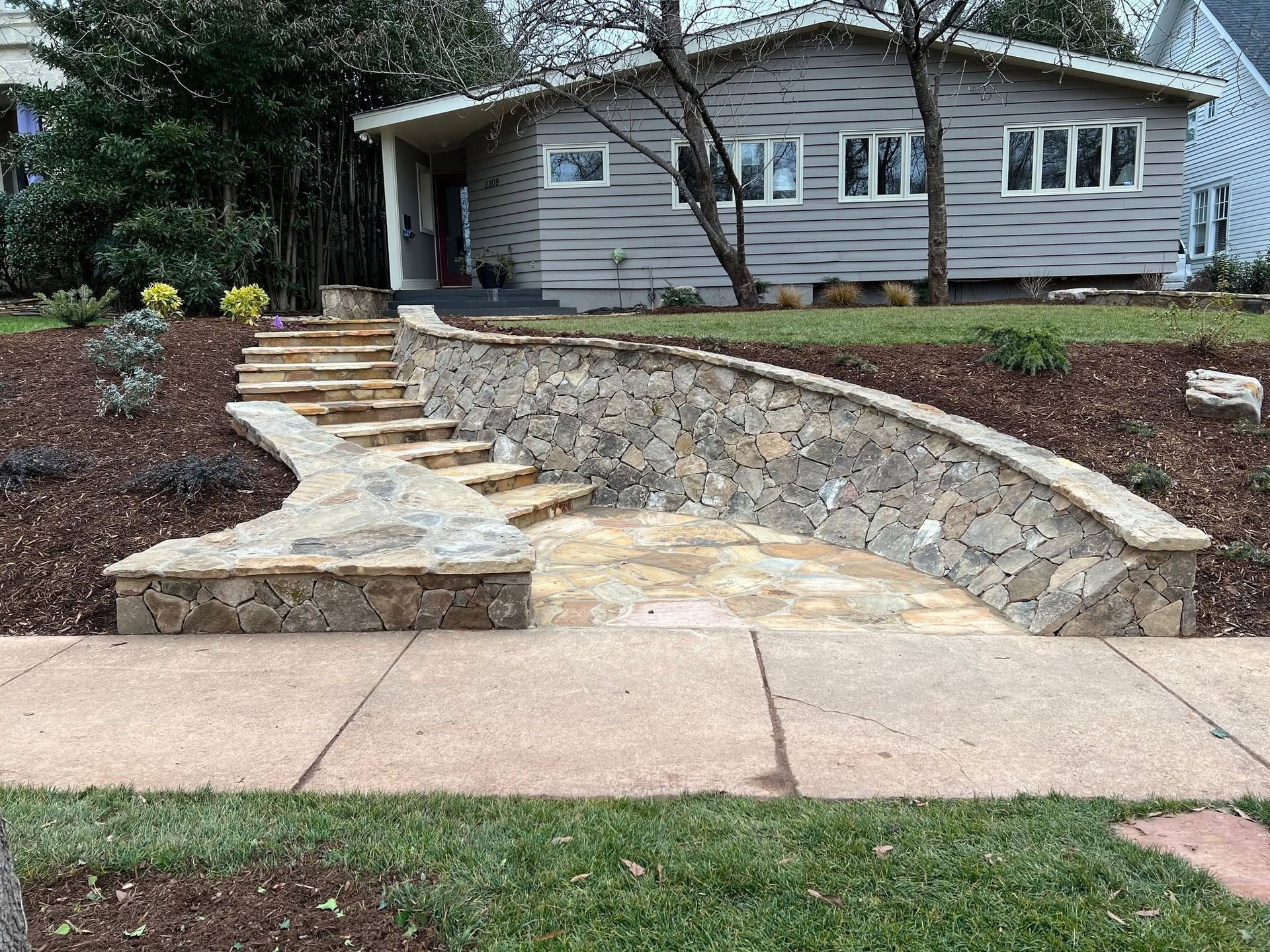 Stone steps and a curving retaining wall leading up to a house with white siding and a front porch