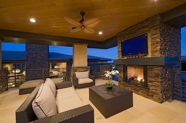 Covered patio with modern seating, fireplace, and stone columns overlooking a scenic view at dusk