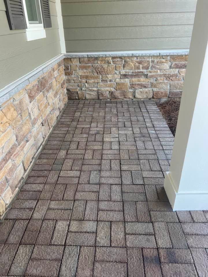 Covered brick patio with herringbone pavers and stone-accent wall beneath a porch