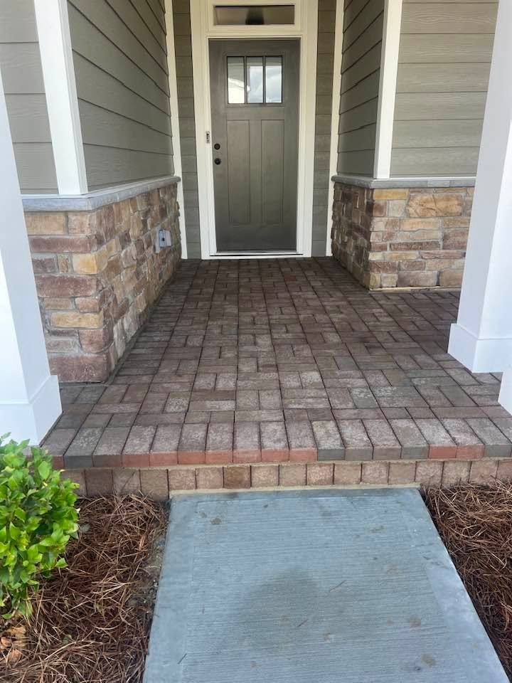 Front porch with brick paver steps, stone-trimmed columns, and a gray front door.