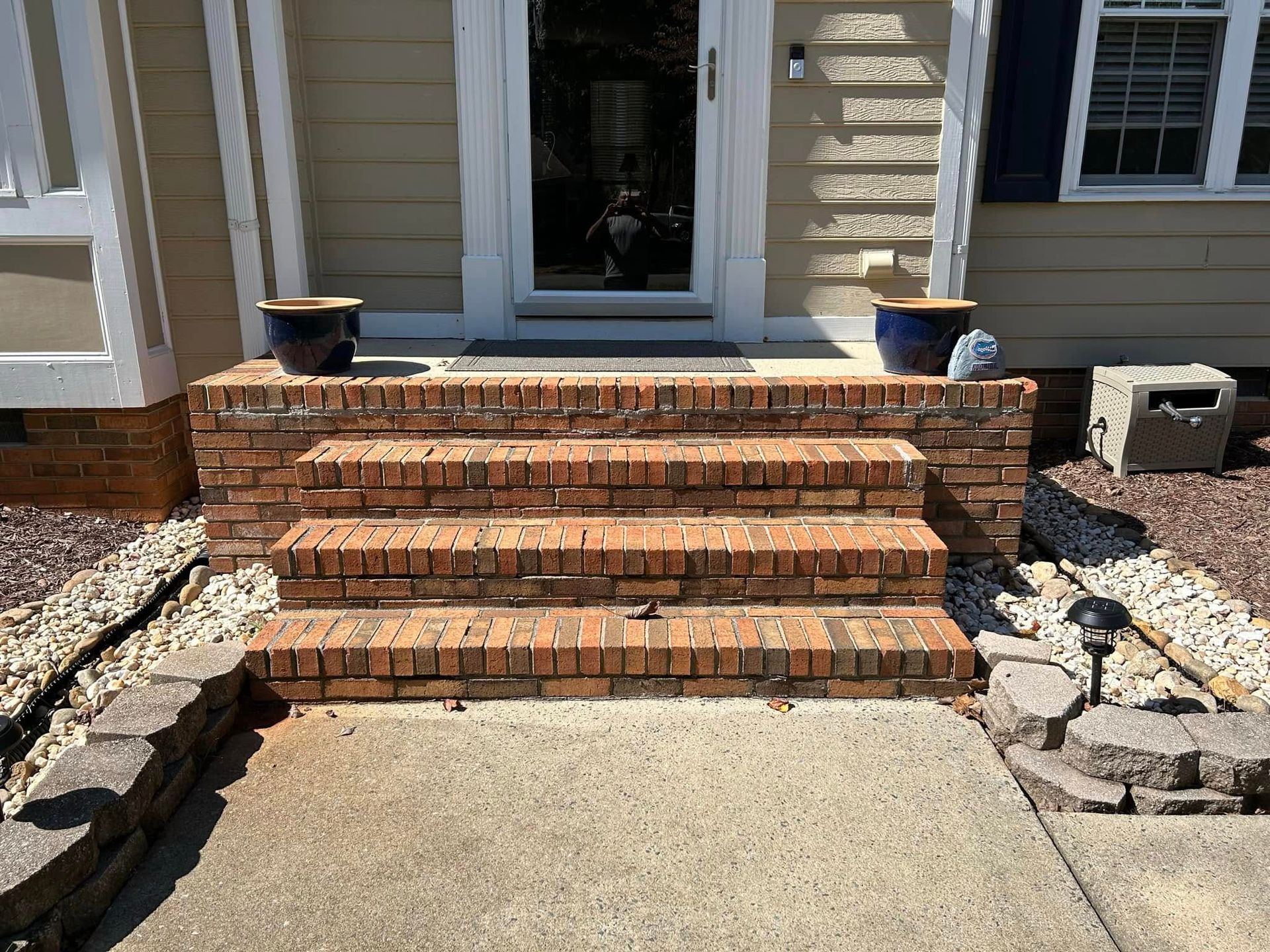 Brick front steps leading to a house entrance, bordered by stone landscaping.