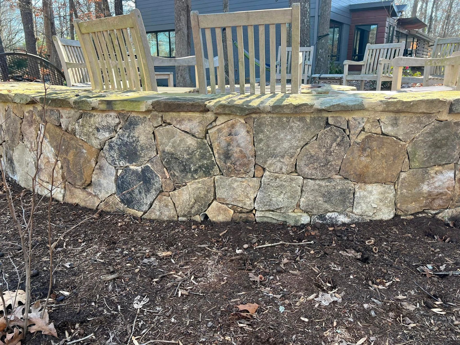 Stone patio wall with two wooden chairs above a mulched garden bed