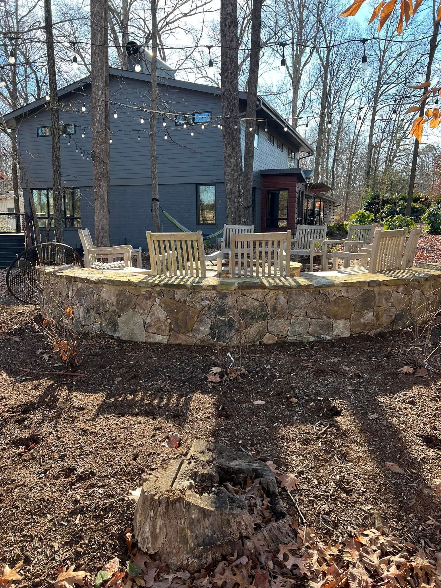 Backyard deck with beige chairs around a stone fire pit in front of a blue house, surrounded by autumn leaves.