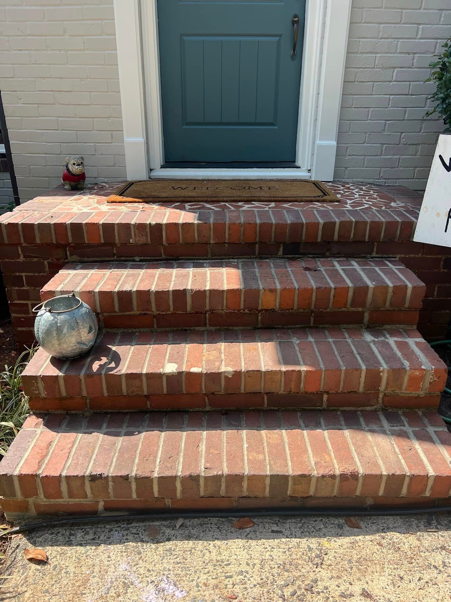 Brick front steps leading to a teal door, with a decorative stone pumpkin on the left side