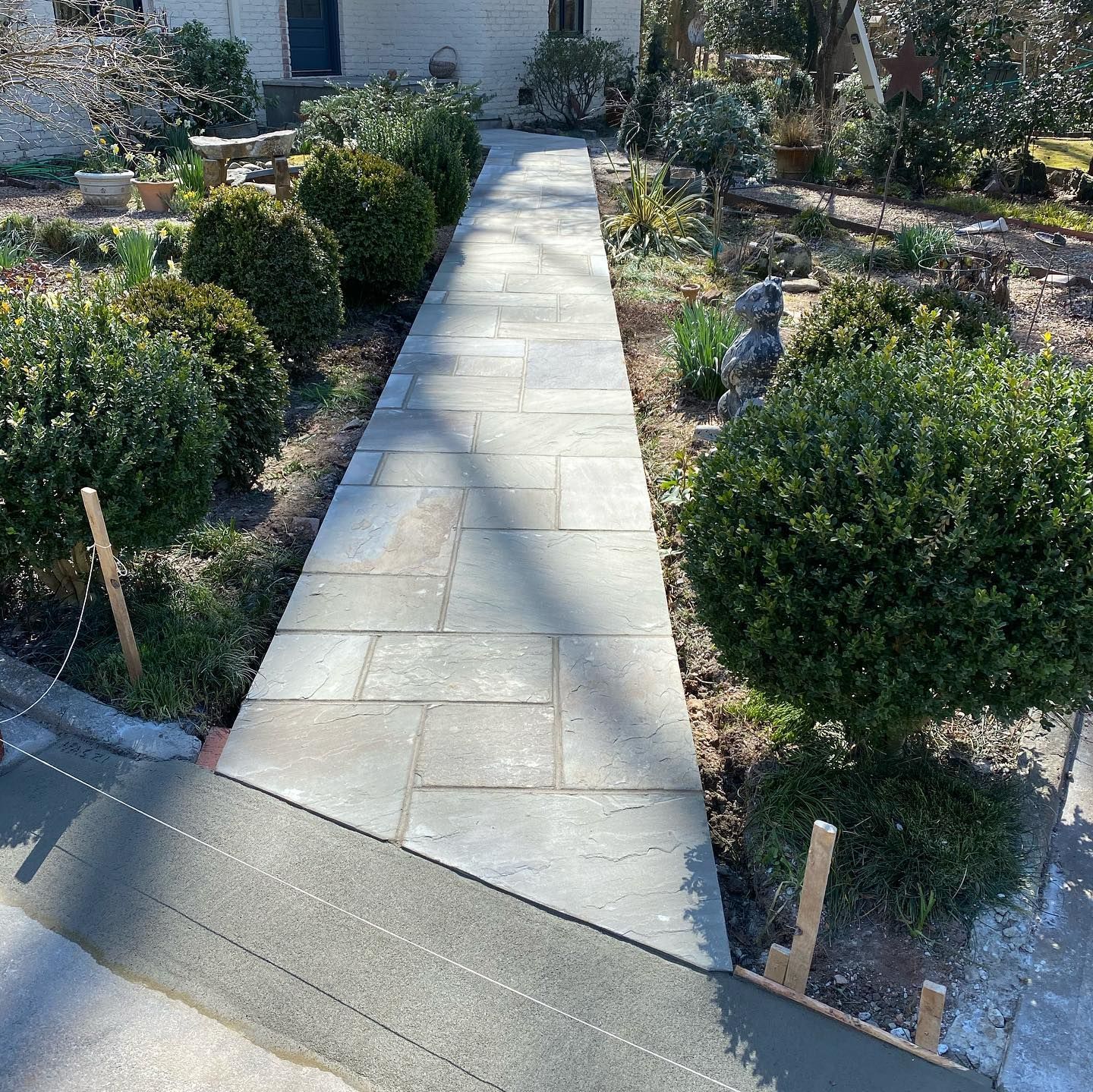 Stone walkway leading to a house through a landscaped garden with shrubs on both sides