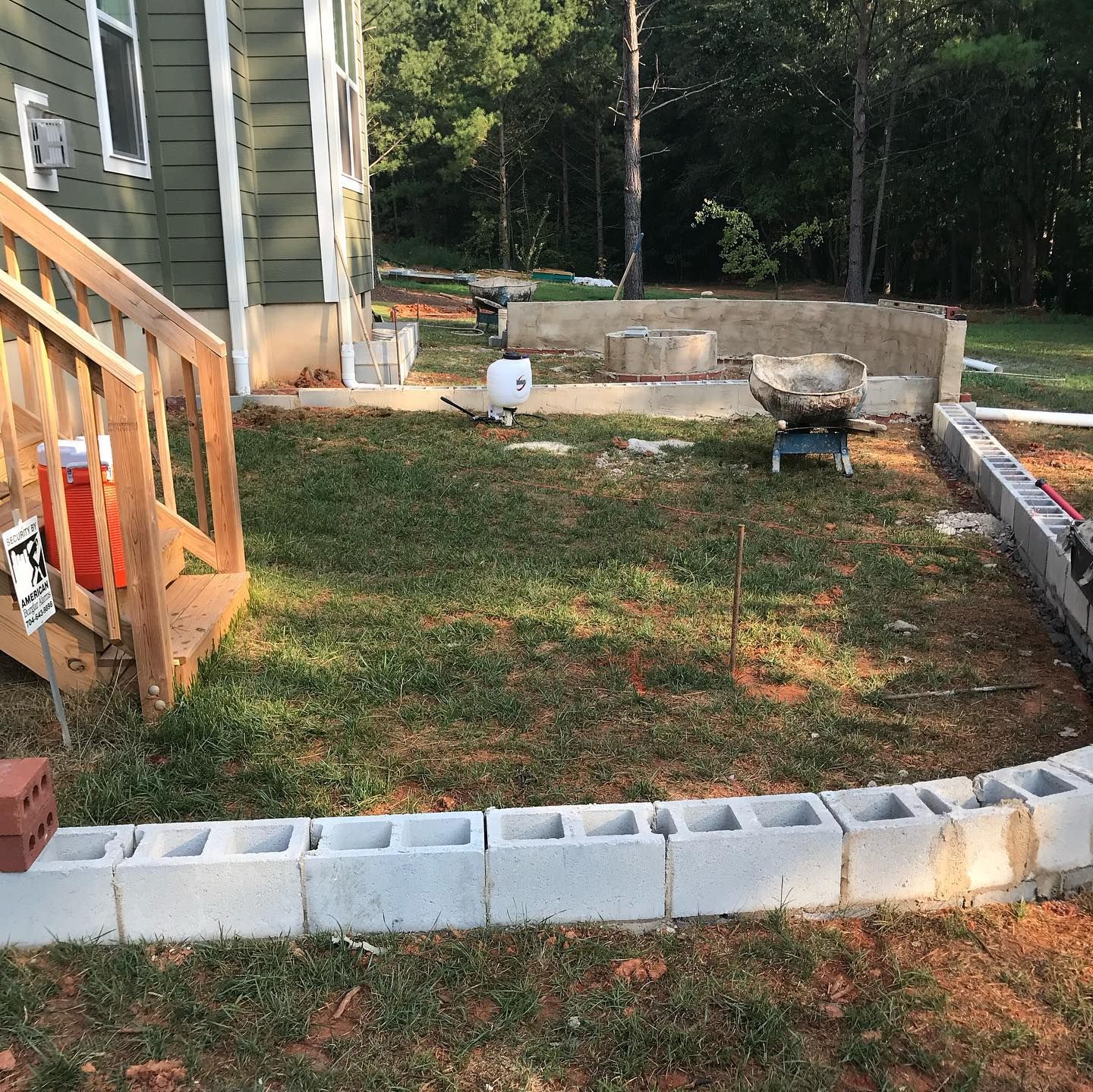 Backyard with a small raised garden bed framed by cinder blocks beside a house and wooden porch steps.