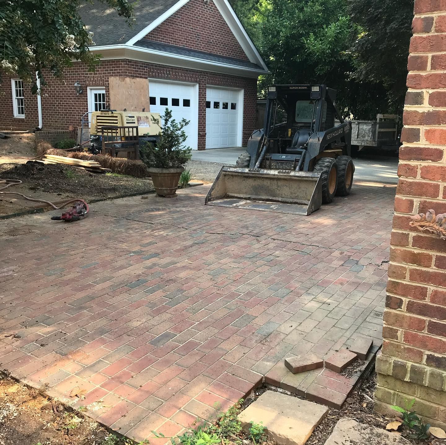 Brick driveway with a front-end loader in front of a brick garage and house.