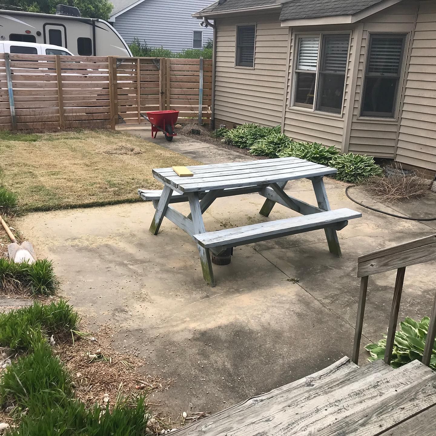 Backyard patio with picnic table, wooden fence, and steps leading to a small garden area.
