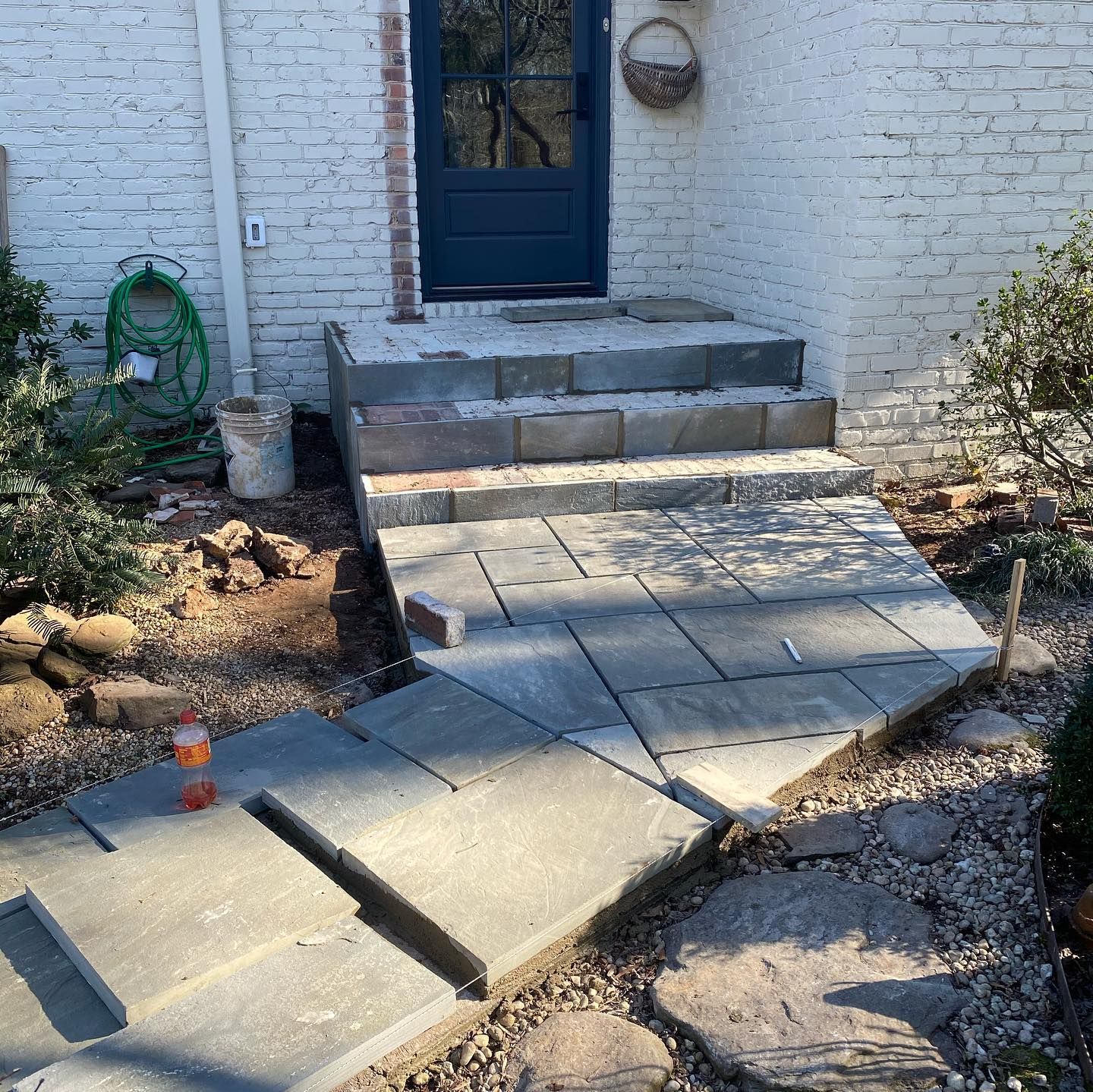 Damaged concrete walkway with shifted slabs leading to a blue front door and steps.