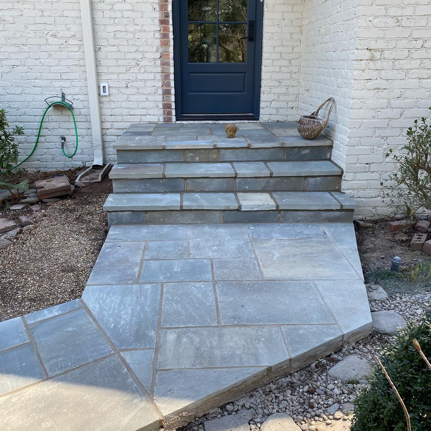 Stone front steps leading to a dark blue door, with a sloped paver walkway and white brick walls