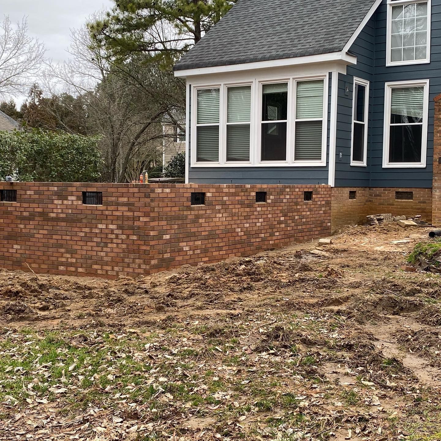 Brick retaining wall beside a blue house with white-trimmed windows and a sloped shingle roof.