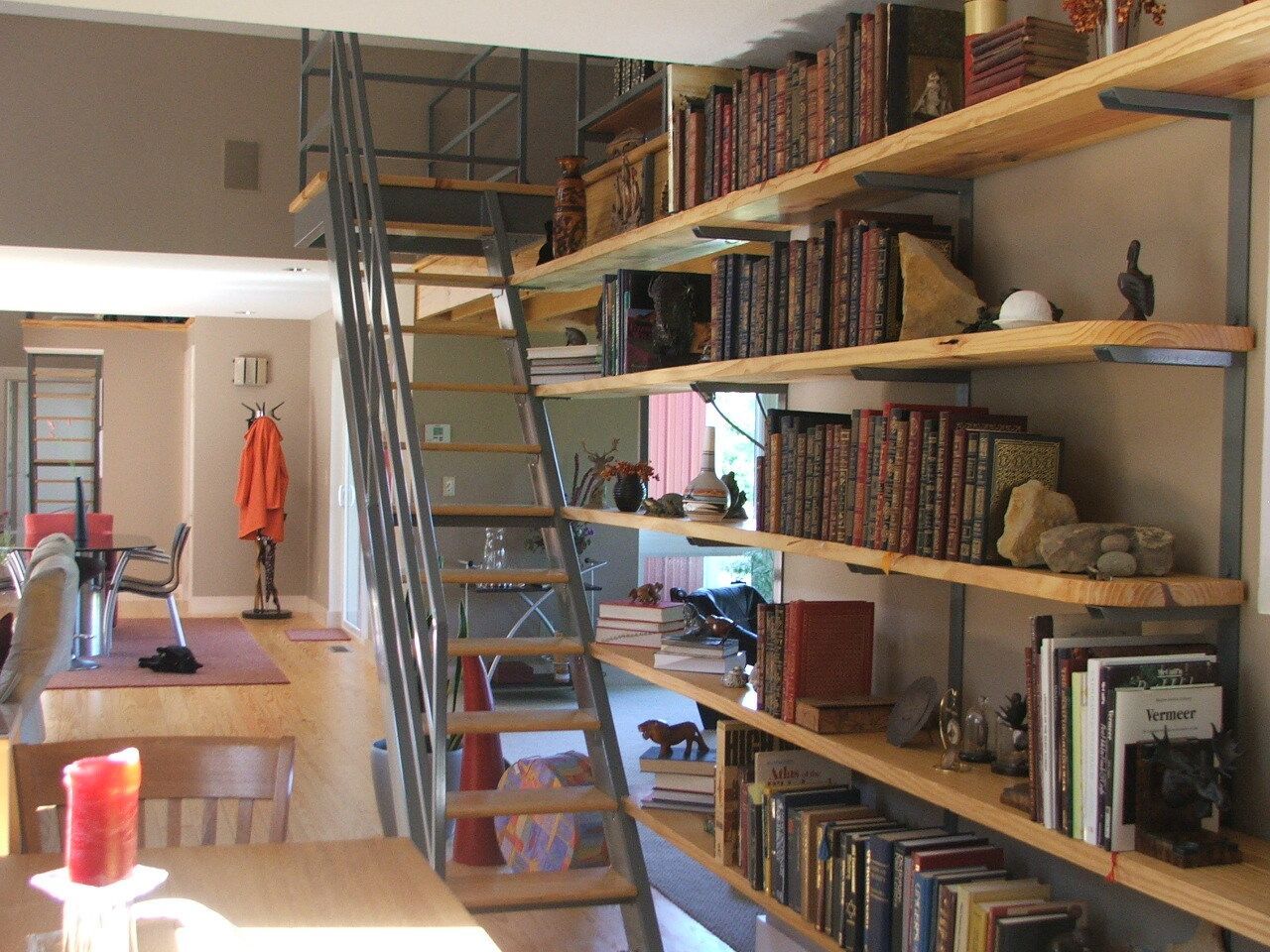Loft interior with tall bookshelves, a metal ladder, and a desk in a narrow, book-lined room.