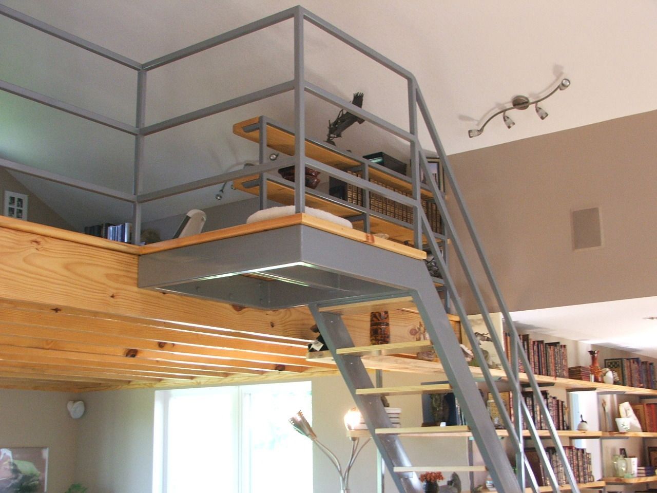 Loft-style room with a gray-railed mezzanine and ladder over a bright living area.