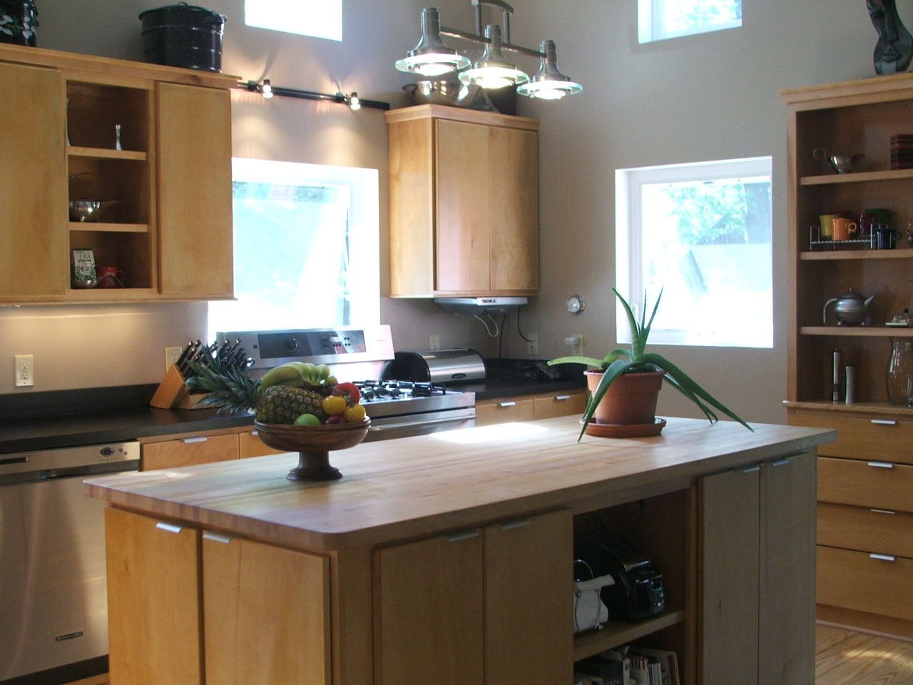 Bright kitchen with wooden cabinets, central island, hanging light fixture, and potted plants by the windows.