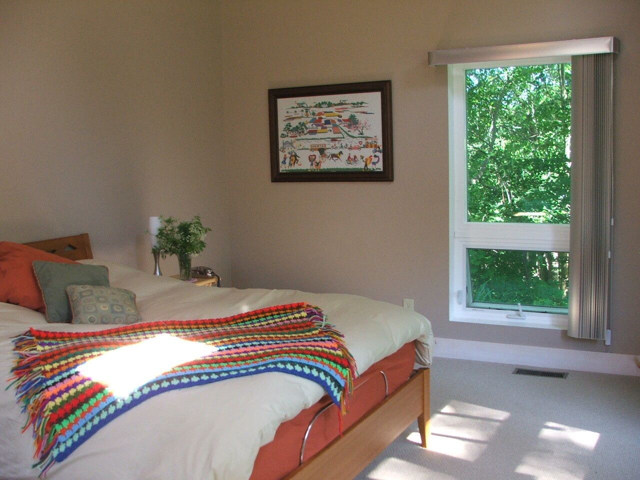 Bedroom with colorful quilted bed, wall art, and a large window showing green trees.