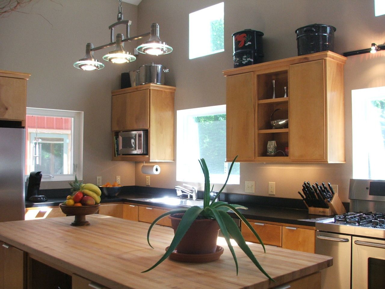 Bright kitchen with wooden cabinets, island table, hanging lights, and potted plant centerpiece.