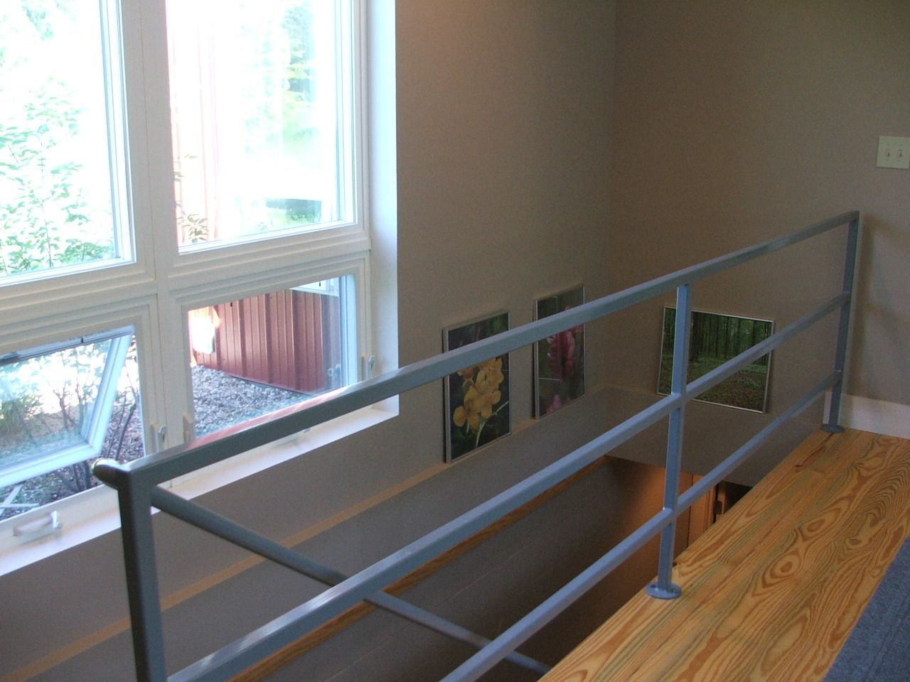 Indoor stairwell with a gray metal railing beside large windows and wood flooring