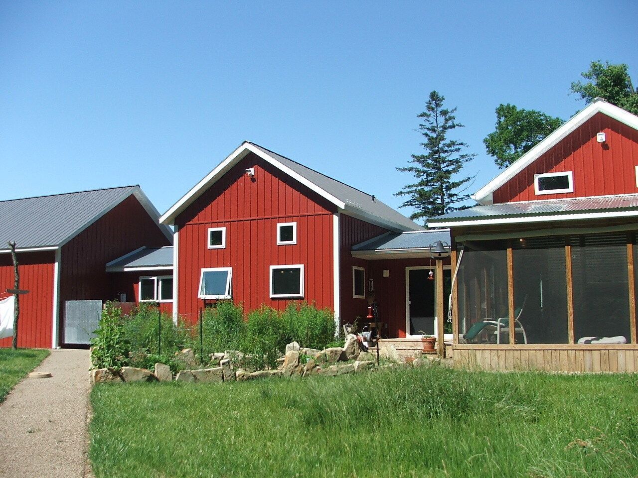Red houses with white trim and a gravel path in a sunny rural yard