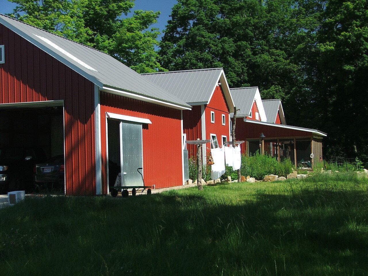 Red barns with white trim beside a grassy yard under bright green trees
