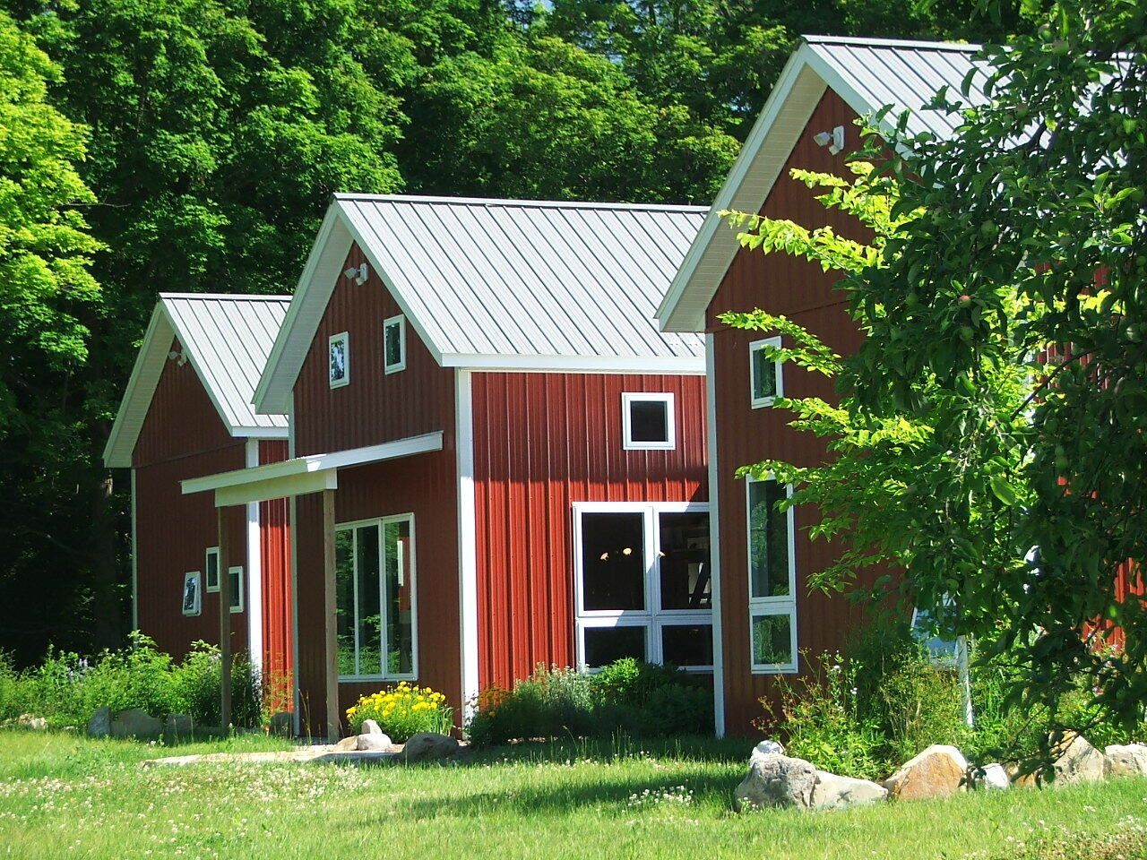 Red house with white trim nestled in lush green trees and grass.