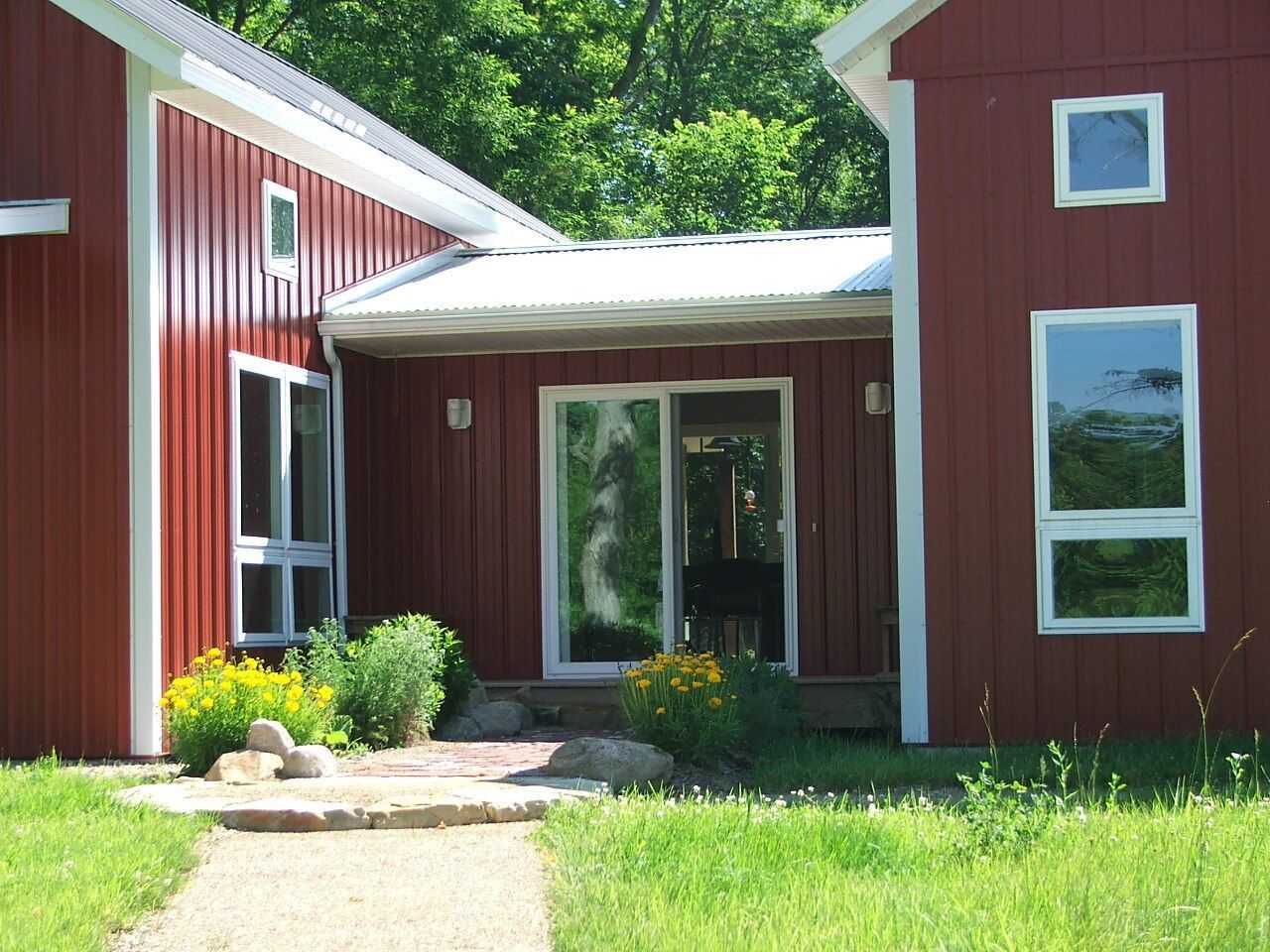 Red house entrance with white trim, glass door, and windows, framed by green lawn and shrubs.