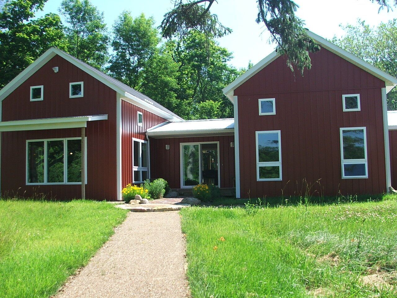 Red house with white trim and a front walkway, surrounded by green lawn and trees