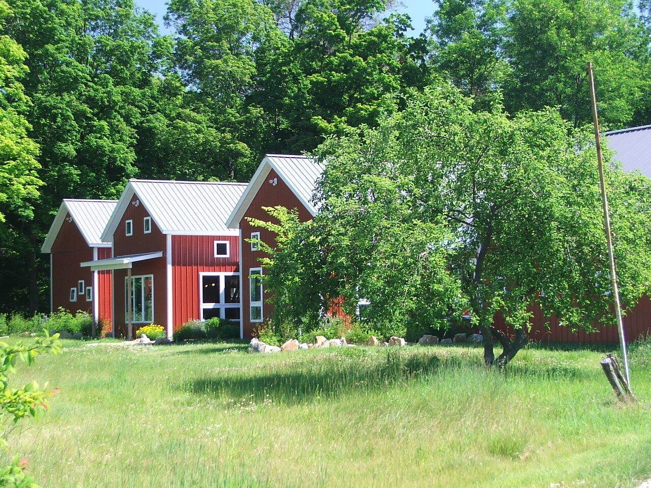 Red cabins among green trees and grass in a sunny rural landscape.