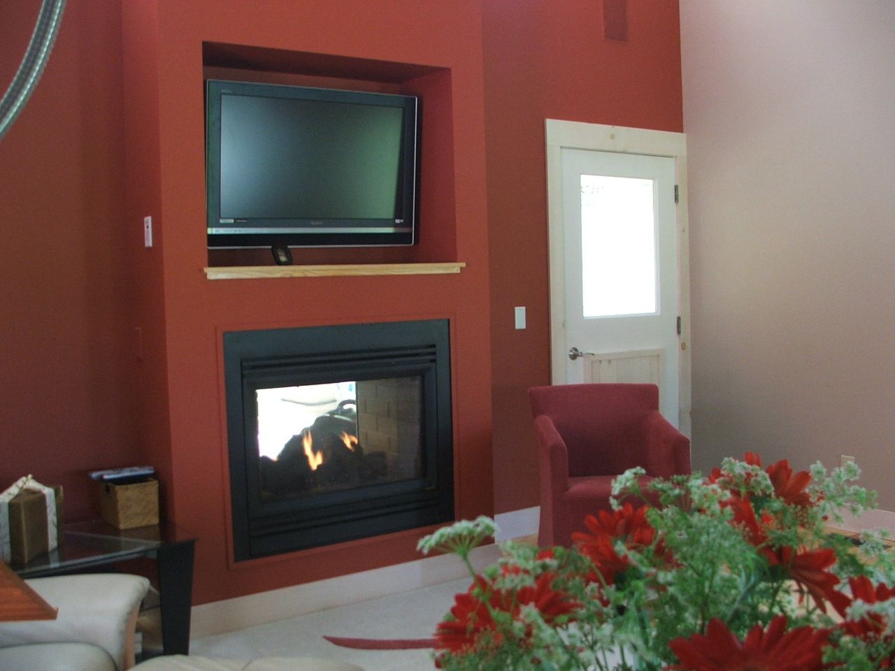 Cozy living room with red walls, fireplace, wall-mounted TV, armchair, and flowers on a table