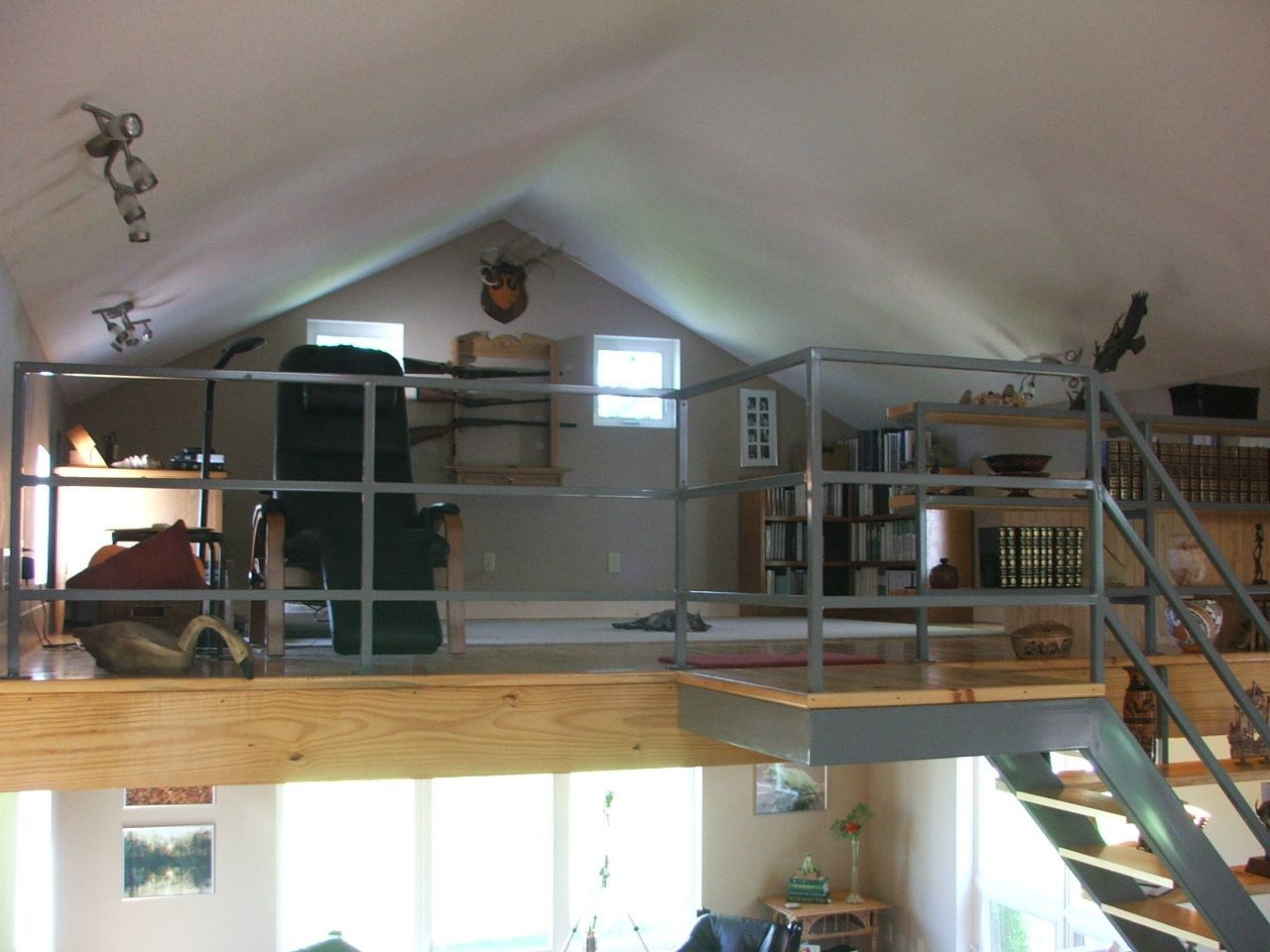 Loft with metal railings, wooden beams, and stairs under a sloped ceiling in an attic space