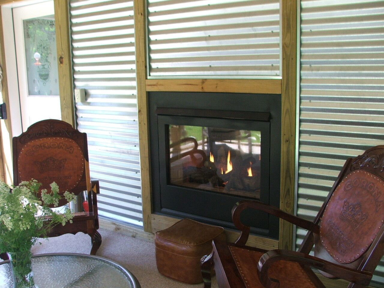 Cozy porch with a fireplace, two wooden chairs, and a small table with plants and flowers.