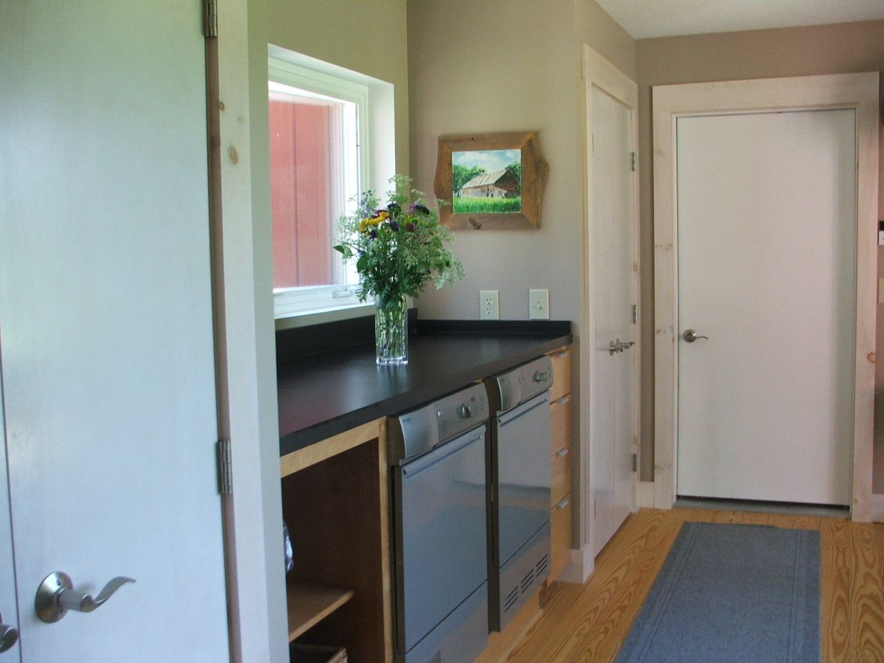 Hallway with dark countertop cabinets, a vase of flowers, and a white door on a runner rug
