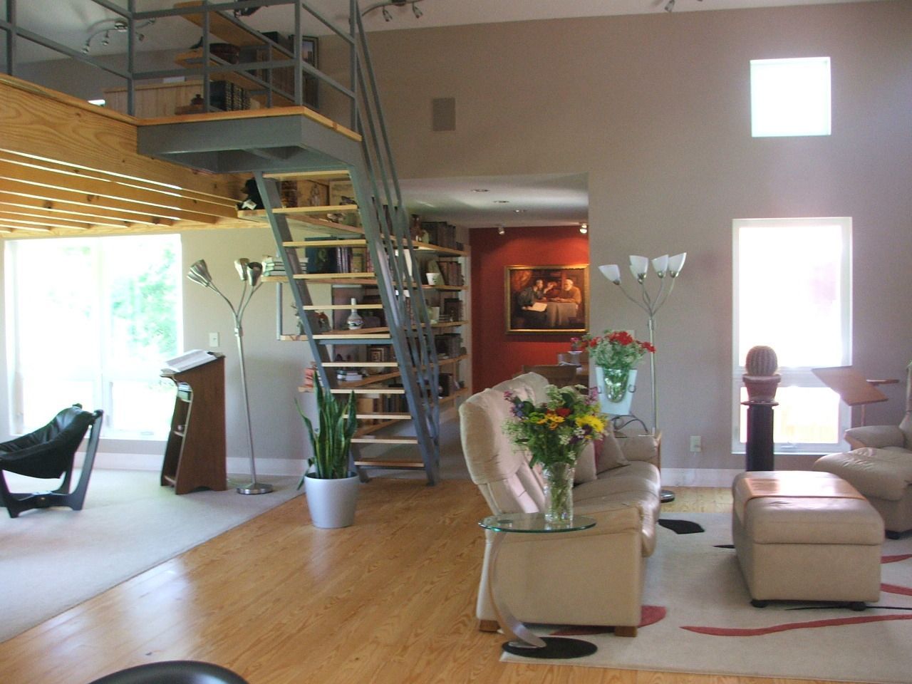 Modern loft living room with wood floors, spiral staircase, beige chairs, and large windows