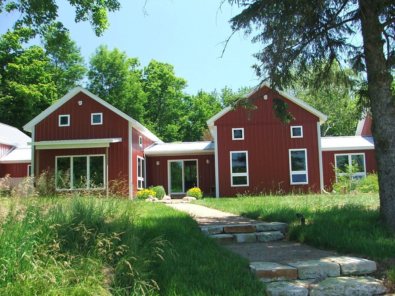 Red houses among tall grass and trees, with a stone path leading to the front door.