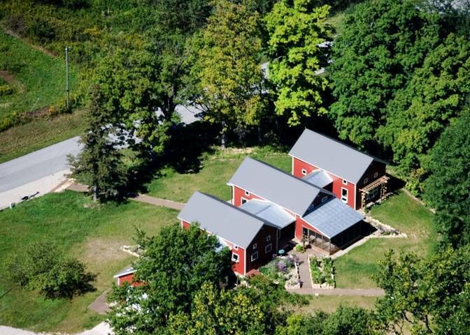 Aerial view of three red barns with gray roofs beside a road and trees