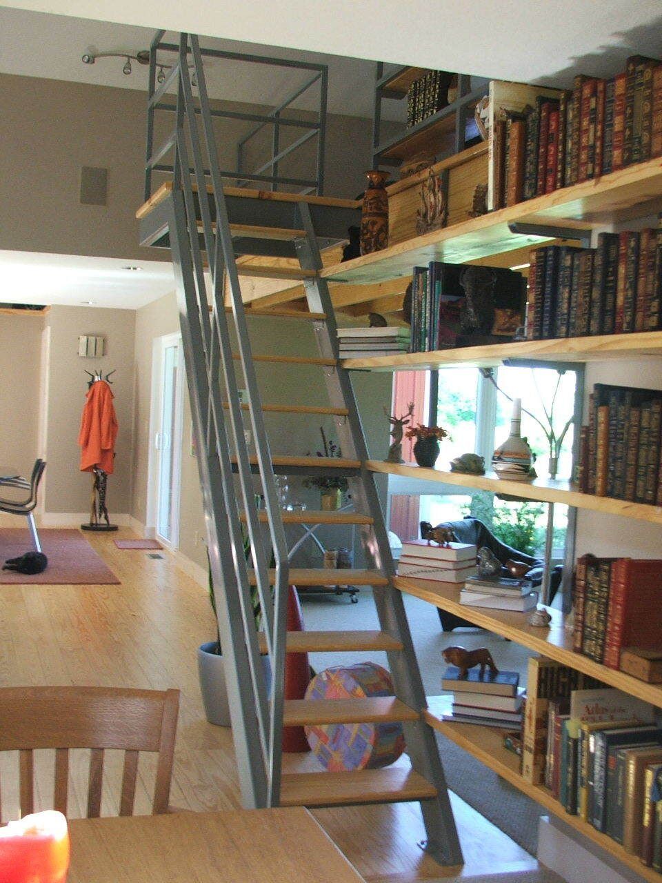 Loft staircase beside tall bookshelves in a cozy home library with a desk and chairs