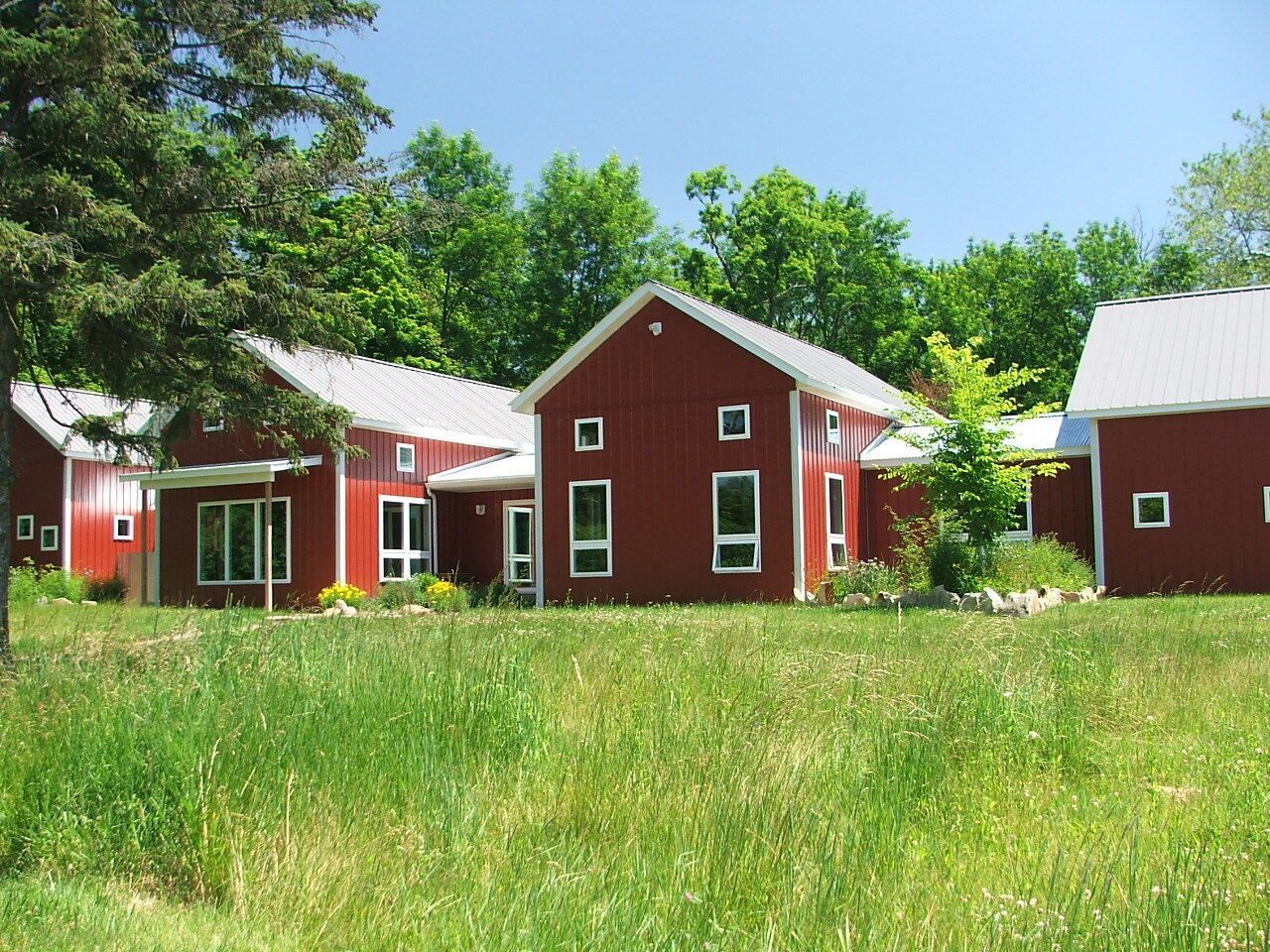 Red farm-style houses with white trim in a grassy field under a blue sky