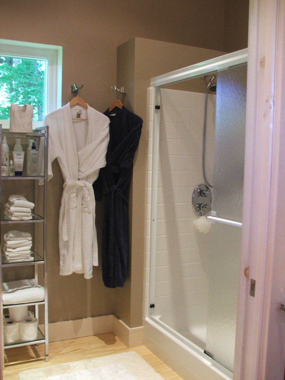 Bathroom with a shower stall, hanging bathrobes, and folded towels on a shelf.
