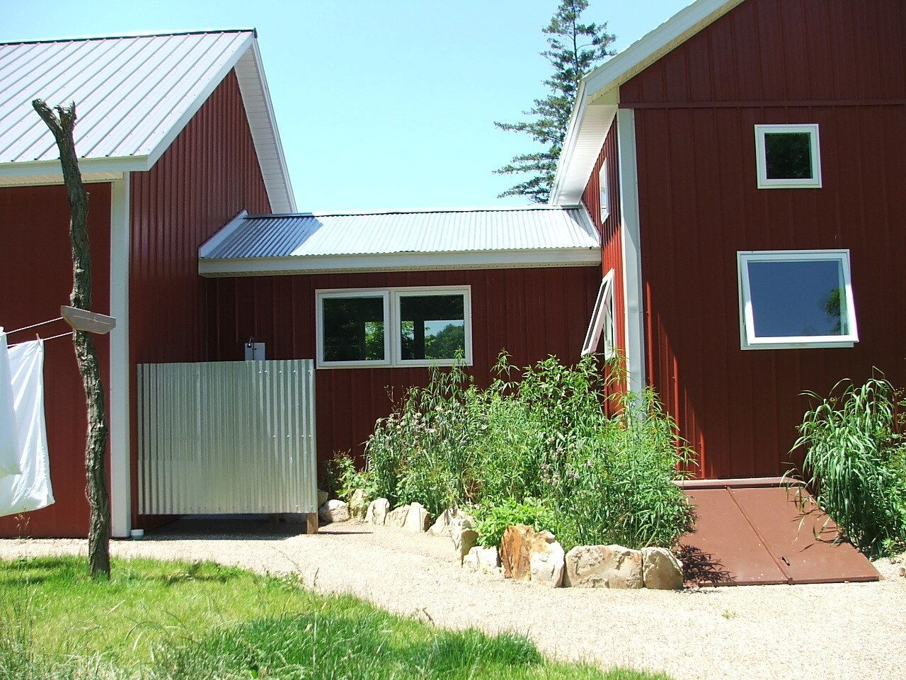 Red house with metal roofs, small courtyard, and green shrubs in front