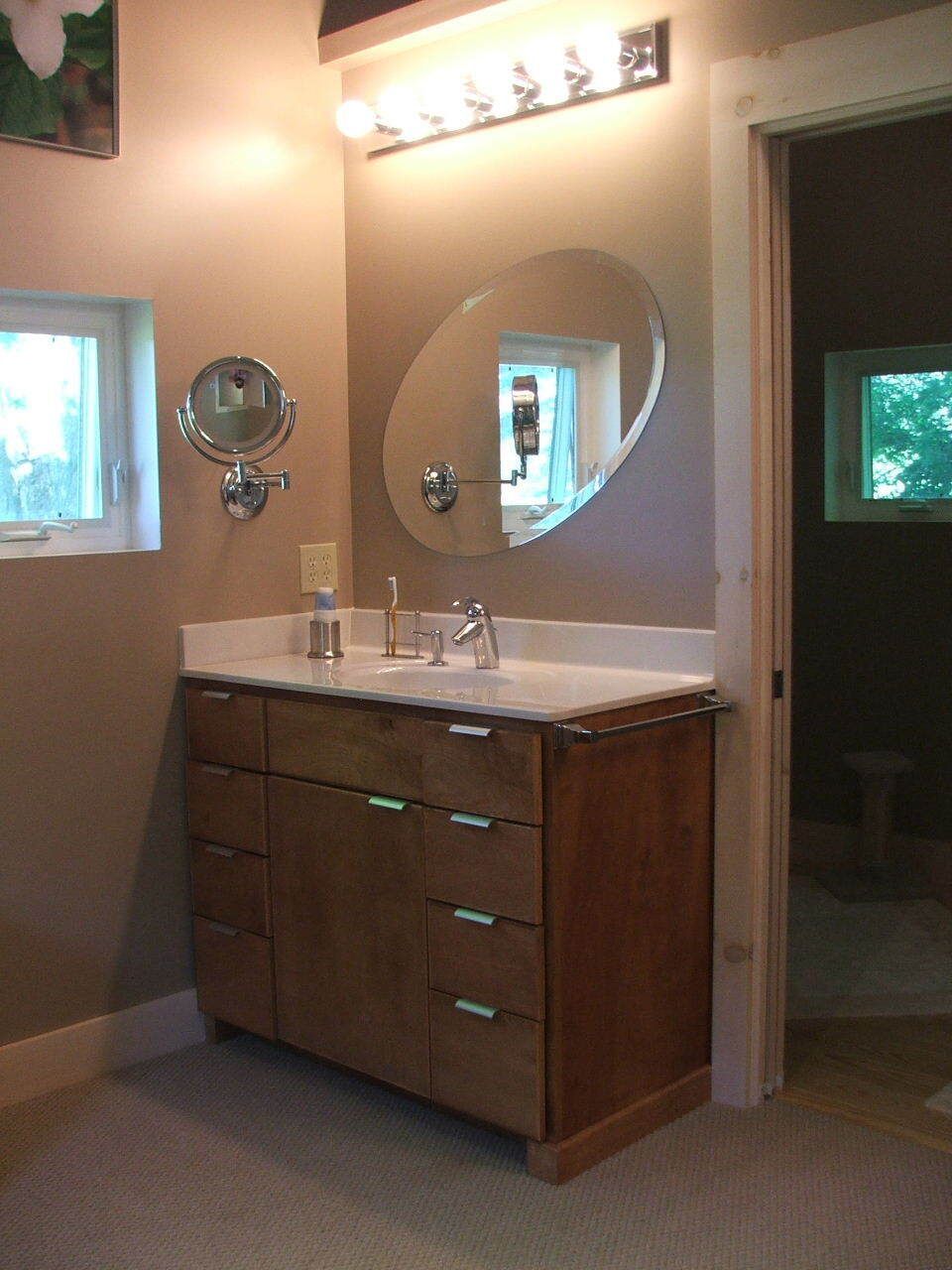 Modern bathroom vanity with wood cabinets, round mirror, sink, and overhead lights