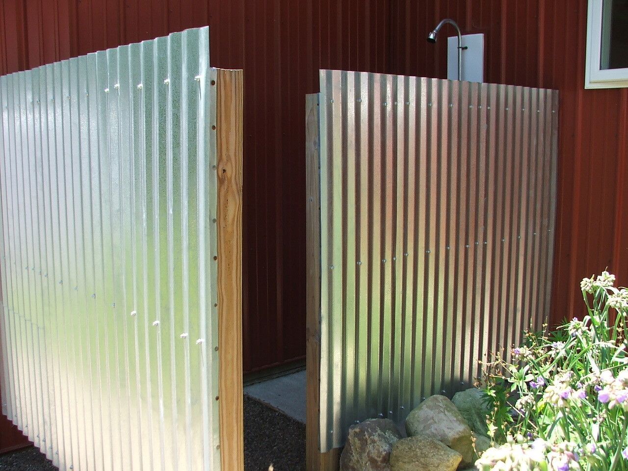 Corrugated metal gate at a garden entrance with red wooden fence and flowers nearby