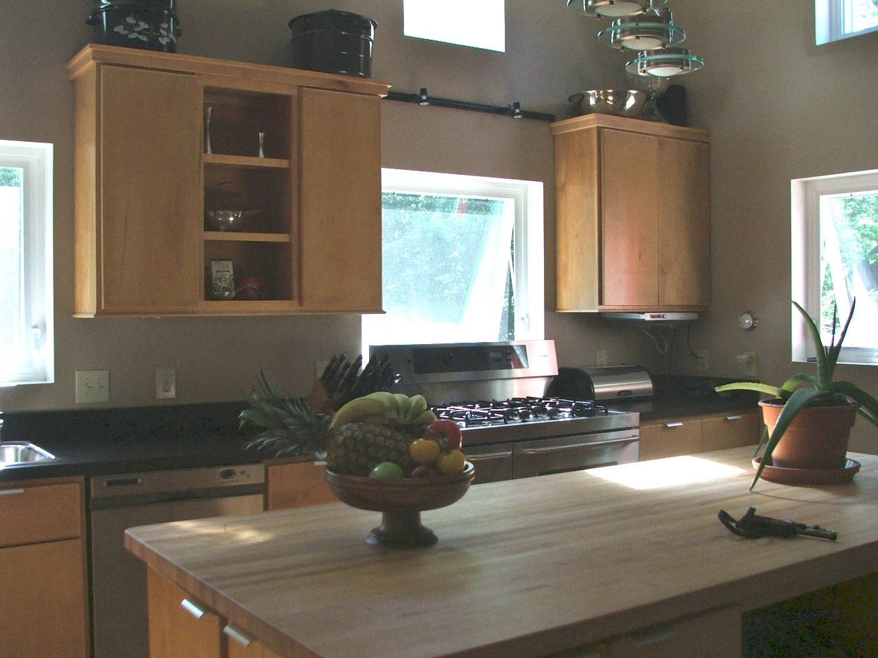 Modern kitchen with wooden cabinets, central island, and large windows letting in bright daylight.
