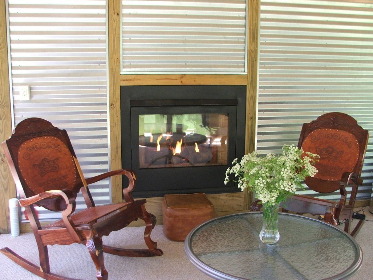 Two wooden armchairs beside a glass coffee table facing a fireplace in a paneled room