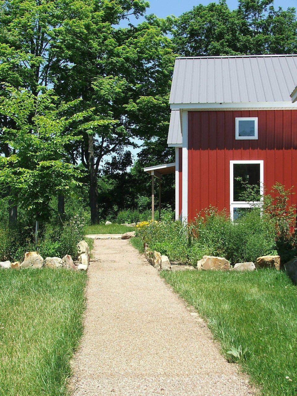 Gravel path leading to a red barn with white trim beside green grass and trees