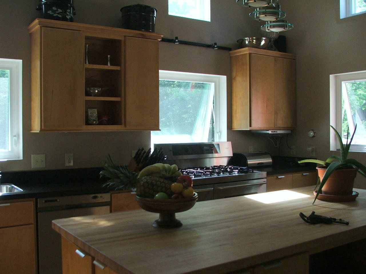 Sunlit kitchen with wooden cabinets, black countertops, and a central island with fruit and plants.