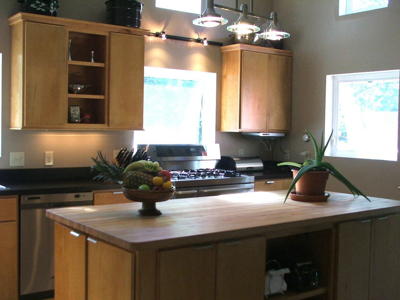 Warm kitchen with wooden island, hanging lights, cabinets, and two bright windows.