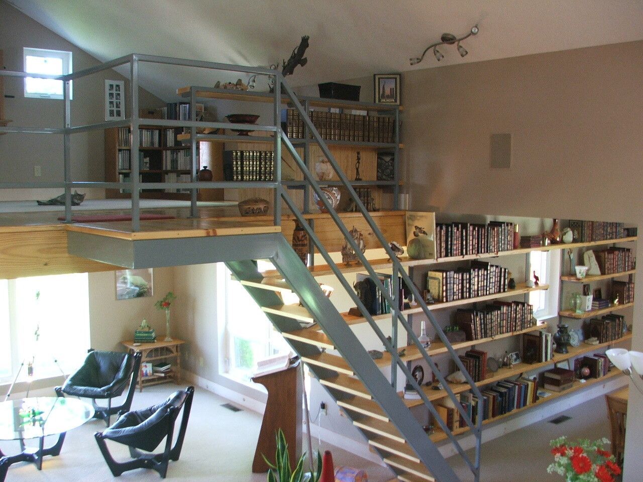 Interior of a loft-style library with a mezzanine, stairs, bookshelves, and seating area below.