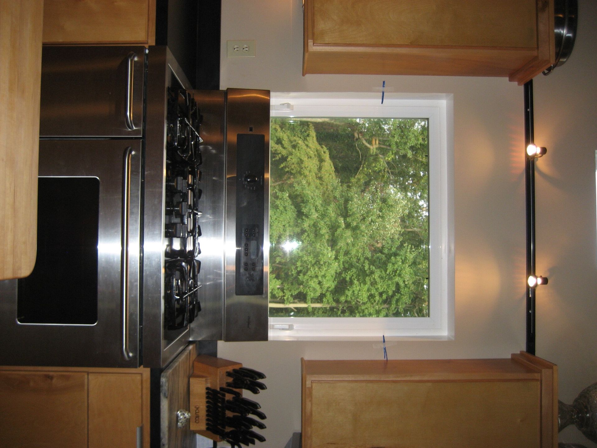 Kitchen with stainless steel stove, wood cabinets, and a window looking out to green trees.