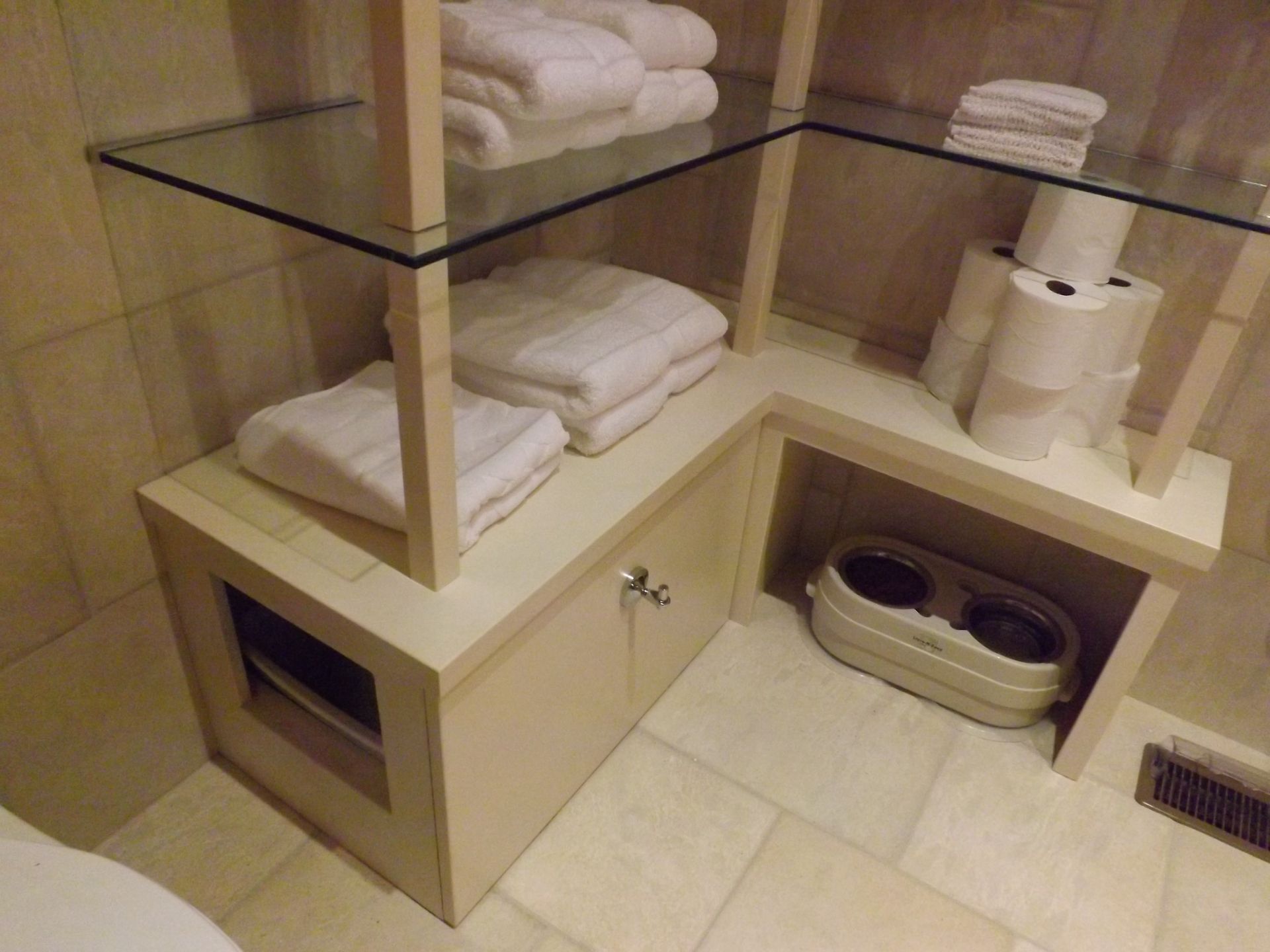 Bathroom with beige tile, folded white towels on shelves, and a toilet tucked under a counter.