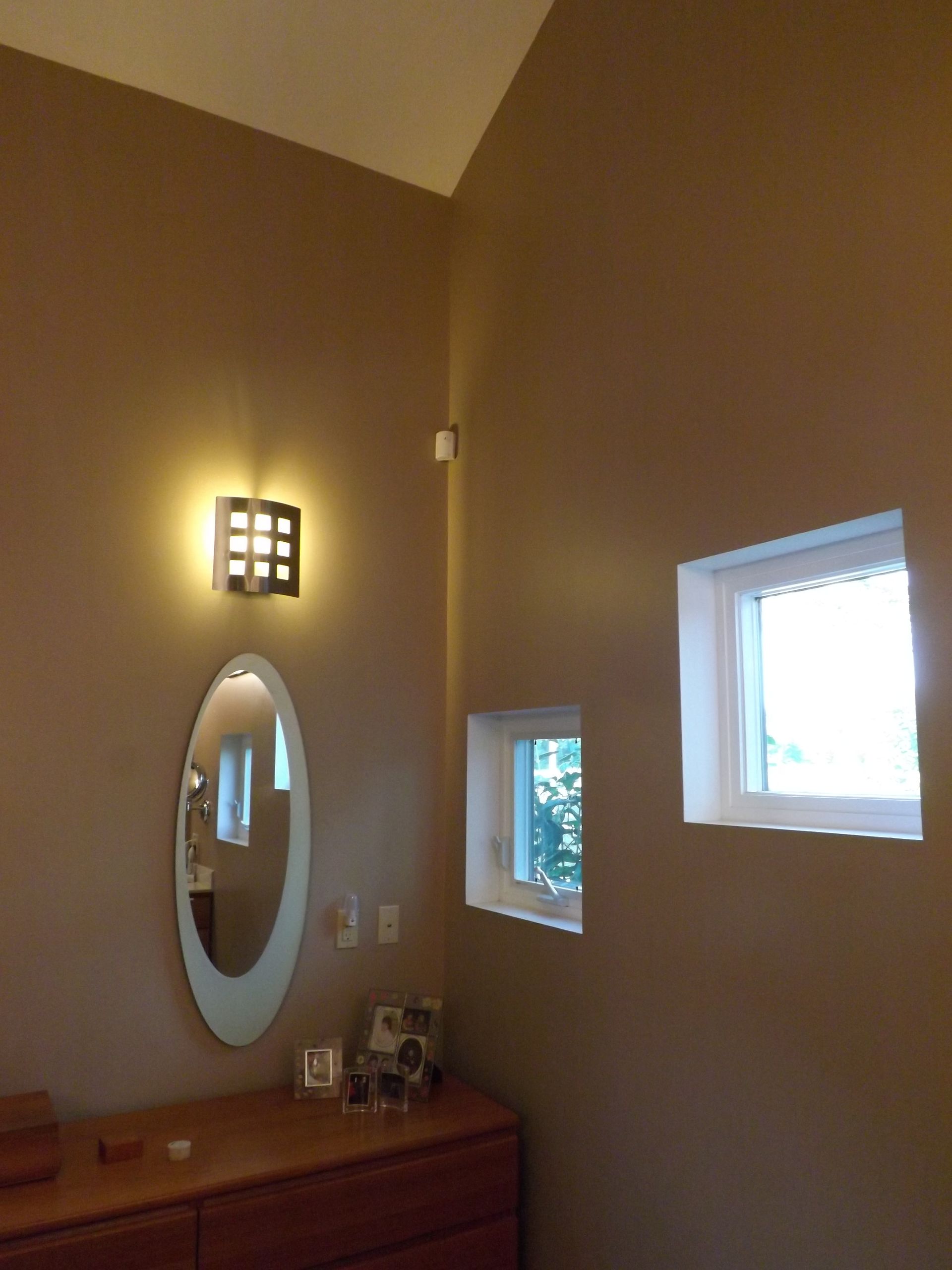 Bathroom vanity with oval mirror, wall sconce, and two small windows in beige walls.